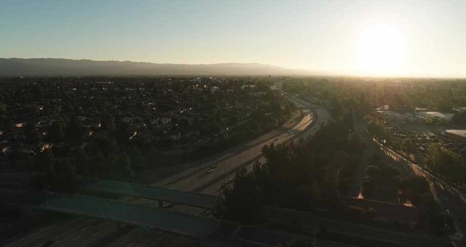 A highway with vehicles buildings trees a mountain range the sky and clouds in the background