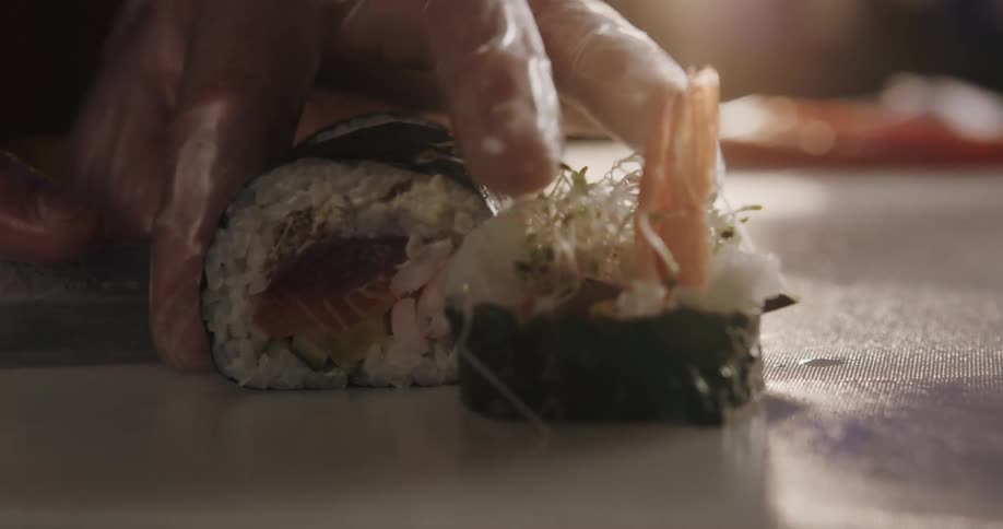 A person with gloves cutting sushi with a knife on a table