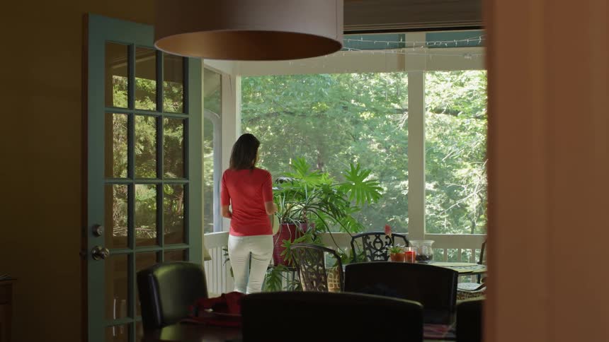 A woman walks from her house to a covered porch to water some plants