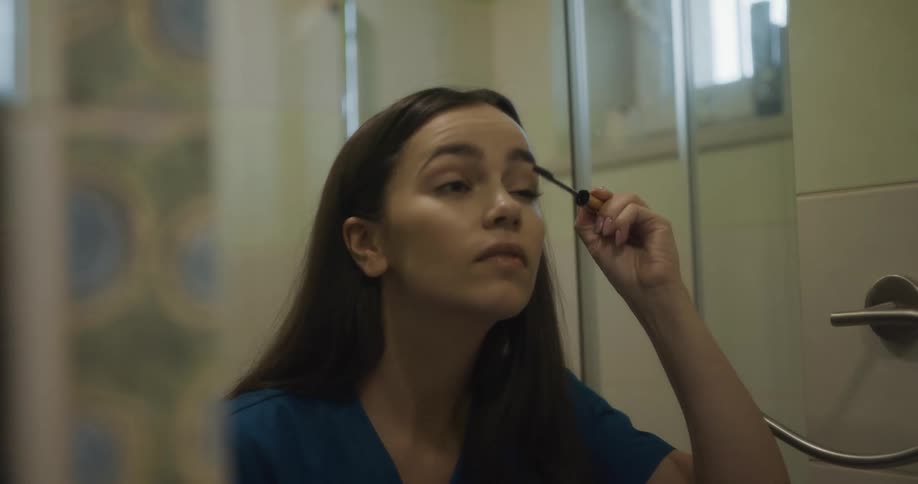 A woman looks in the mirror at home and puts on mascara