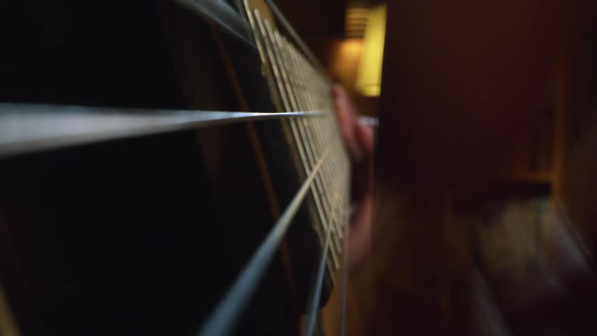 A person in a room playing a guitar with a lamp and a wall in the background