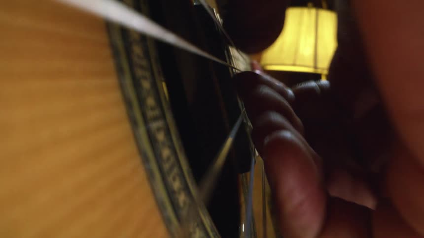 Person is playing an acoustic guitar and strumming the strings with their fingers