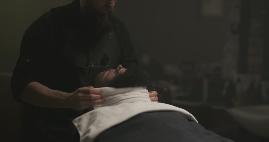 A barber wrapping a towel around a clients beard