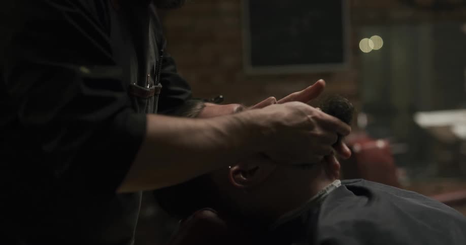 A man in a barbershop applying oil to another mans beard