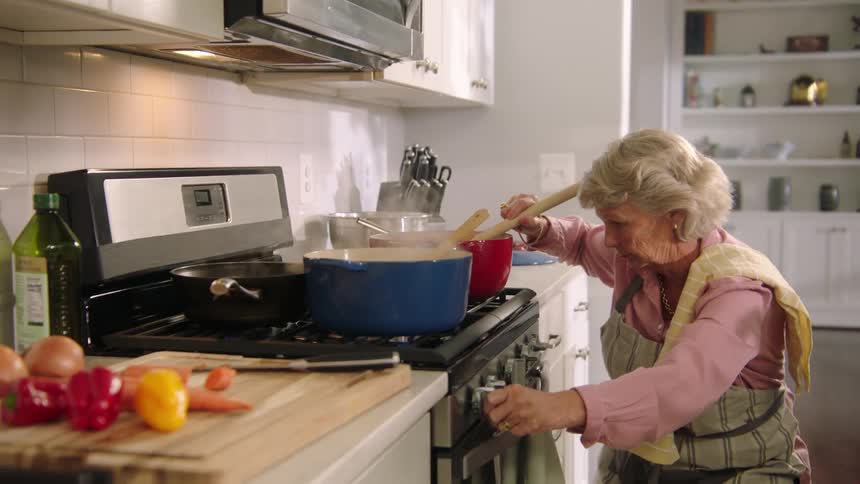 A woman with a apron in the kitchen stirring a pot on the stove