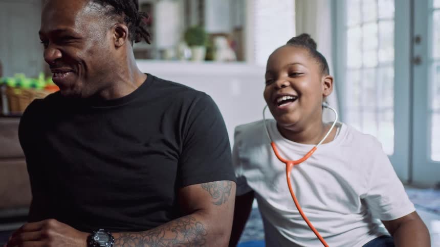 A man laughs while sitting on a rug next to a pair of girls wearing stethoscopes around their necks