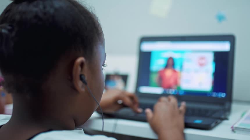 A girl in a room sitting on a desk typing on a laptop