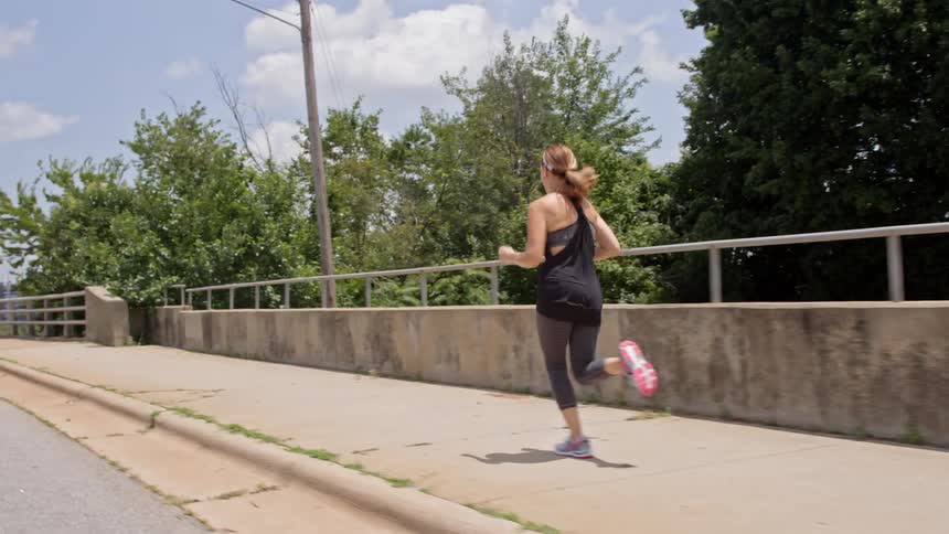 A woman jogs over a bridge during the day