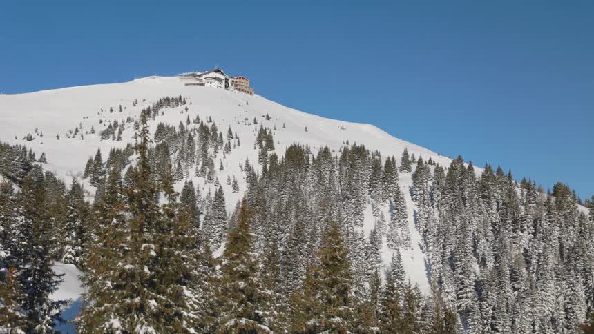 House on top of a snow covered mountain with a forest of pine trees below on a clear day