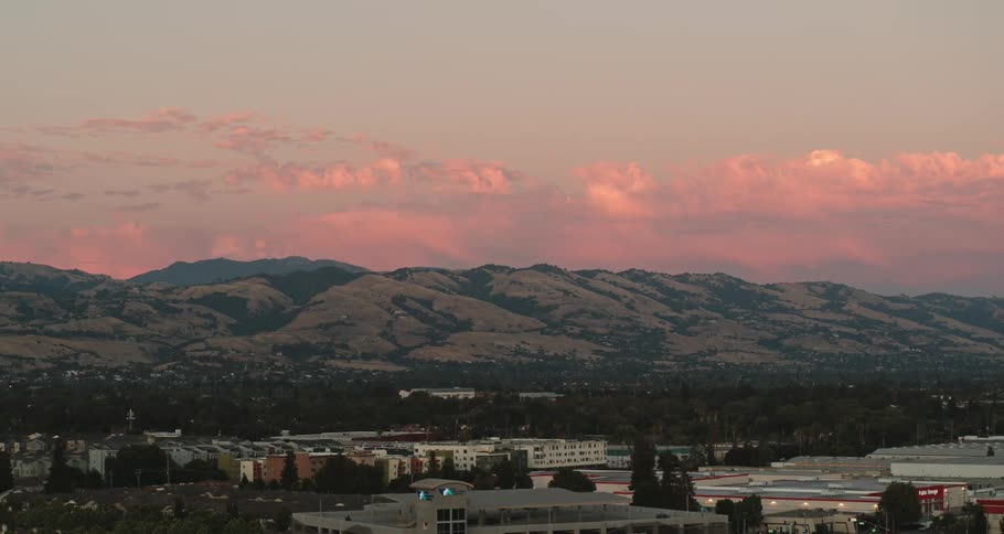A town with buildings and trees with a mountain range the sky and clouds in the background