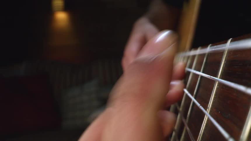 Person playing an acoustic guitar and fingers moving across the frets