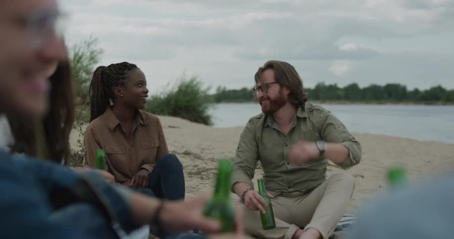Group of friends sitting together chatting and drinking beverages next to a river
