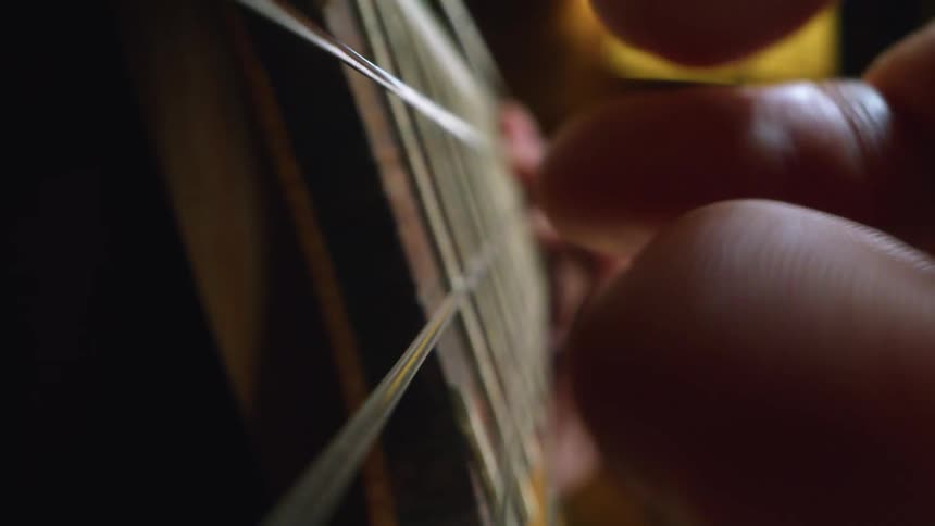 Tight shot of two people plucking strings on a guitar