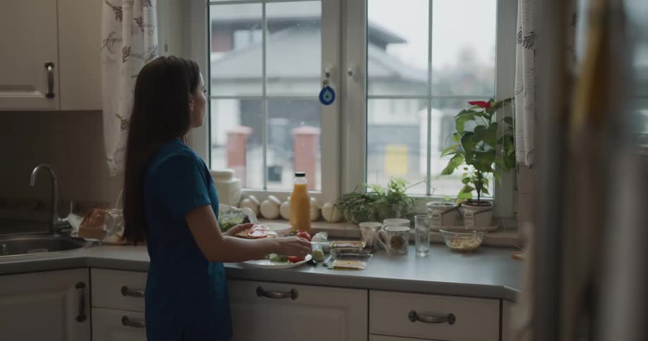 Woman puts together meal standing in kitchen near window
