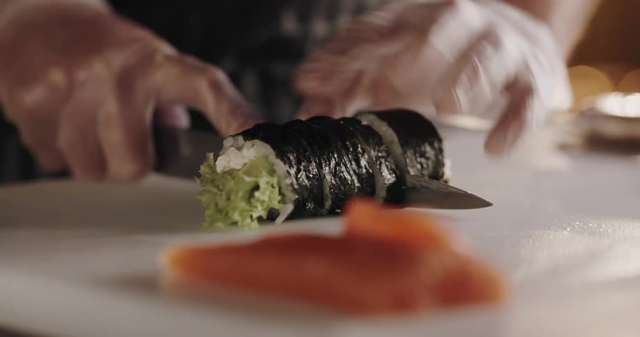 A man with gloves on cuts sushi