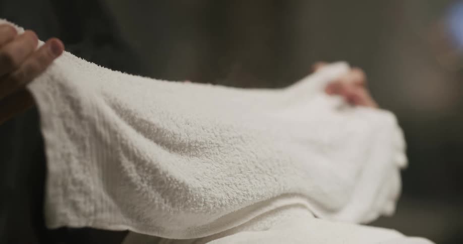 A man in a barbershop putting a hot towel with smoke over another mans face