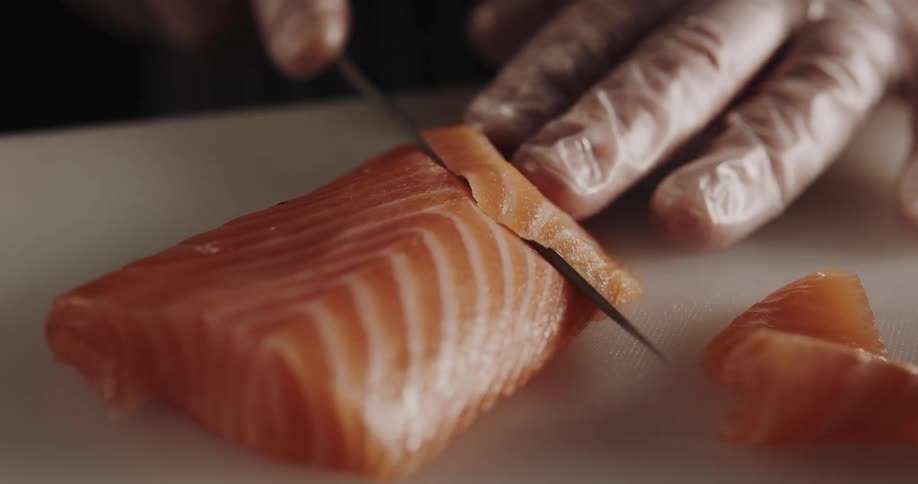Hands slice salmon into thin pieces for sushi sashimi