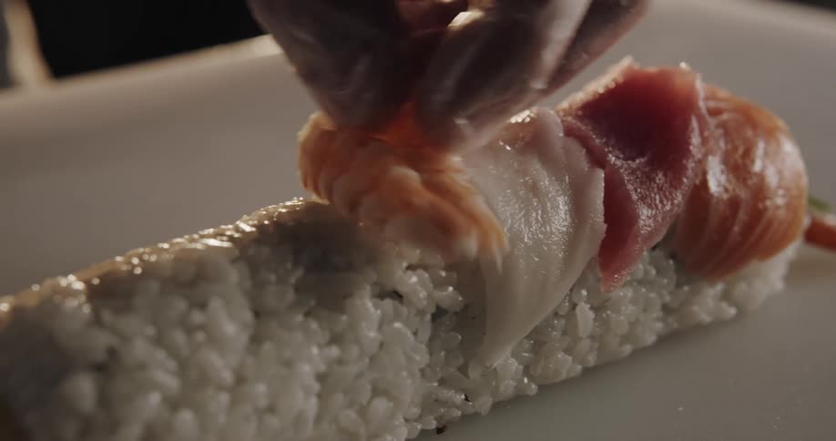 A sushi chef is placing fish on the roll of rice