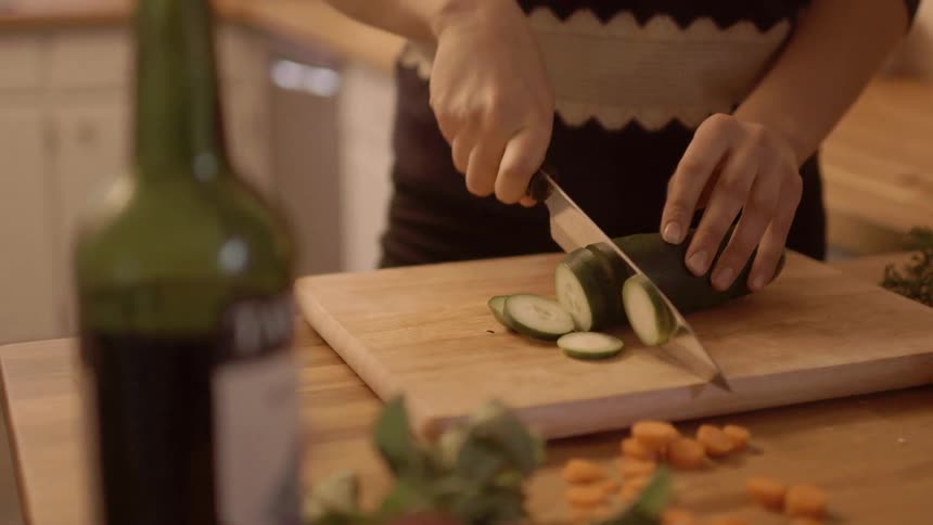 A woman is cutting a cucumber on a board