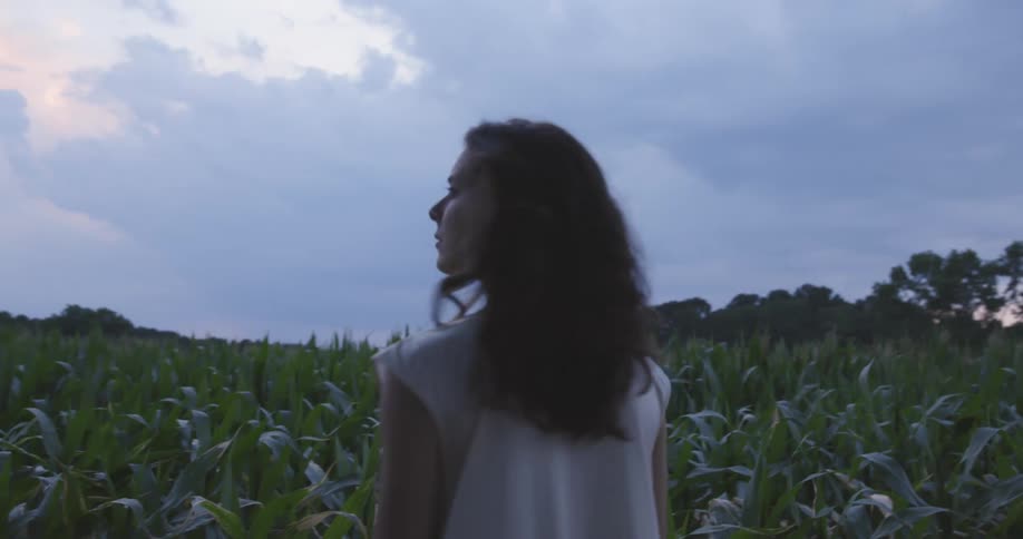 Female walking through cornfield then stops and turns her head around to look behind her