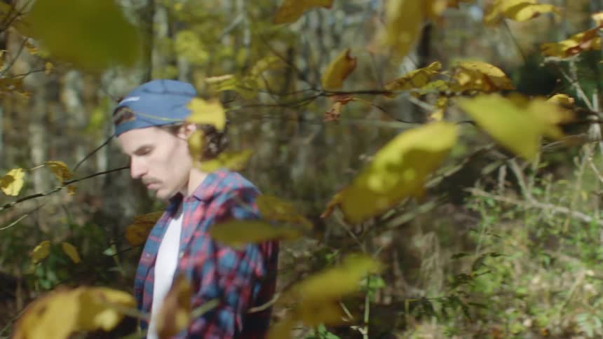 A man with a hat walking in a forest with trees with the sky and clouds in the background