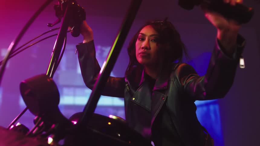 Asian woman wearing a jacket sitting at a motorcycle in front of a big screen posing for a photo shoot