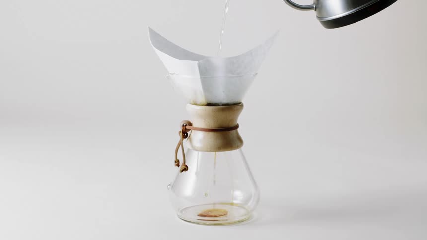A kettle pouring water on a coffee filter over a jar with a white background