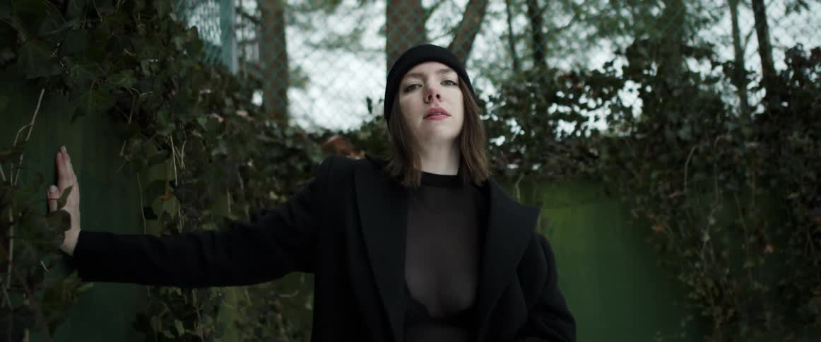 Woman in a toque with her hand placed against a wall with green vines hanging from it