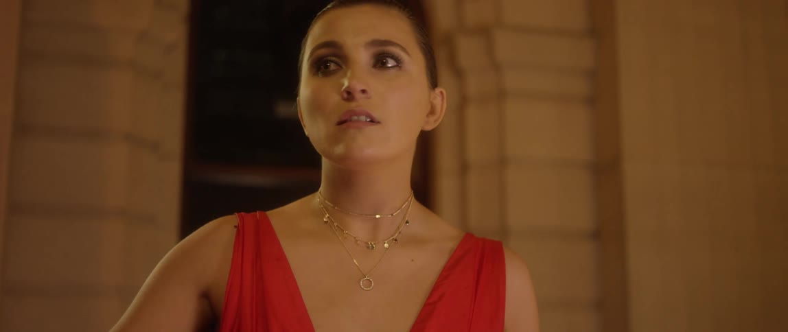 A woman with a necklace and a red dress walking with a building in the background