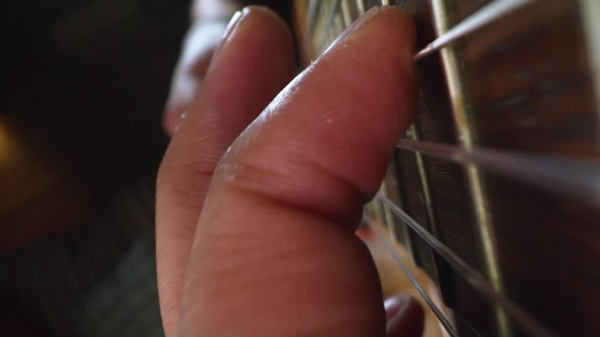 Guitarist is playing an acoustic guitar and moving his fingers across the strings and frets