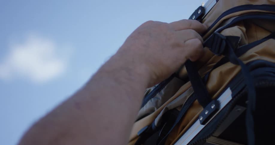 A person loosening a strap with the sky and clouds above