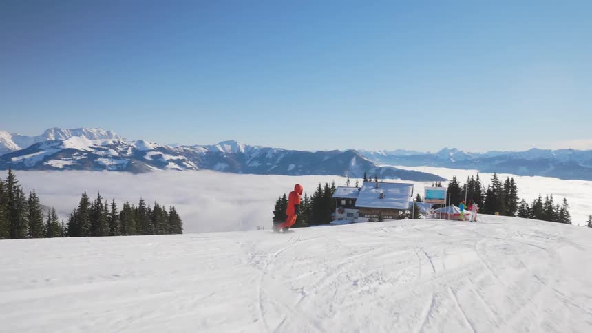 A person with a coat and gloves snowboarding down a snowy slope with a mountain range the sky and clouds in the background