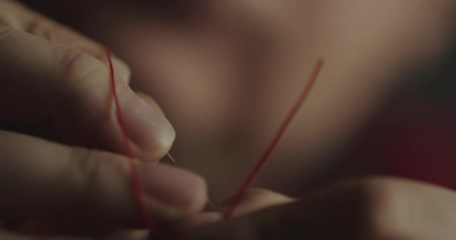 A person putting a string through the eye of a needle