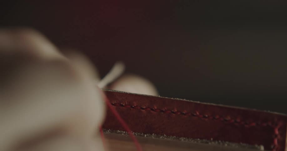 A person is threading a piece of leather