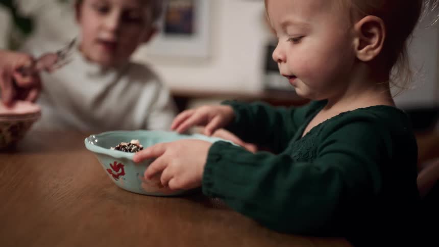 A woman slides a bowl filled with cake over to her daughter as her son sits and waits nearby