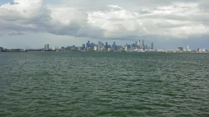 A body of water with the city skyline with buildings and skyscrapers with the sky and clouds in the background