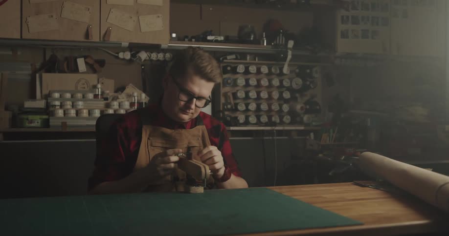 A man with glasses and an apron sitting on a chair in a workshop