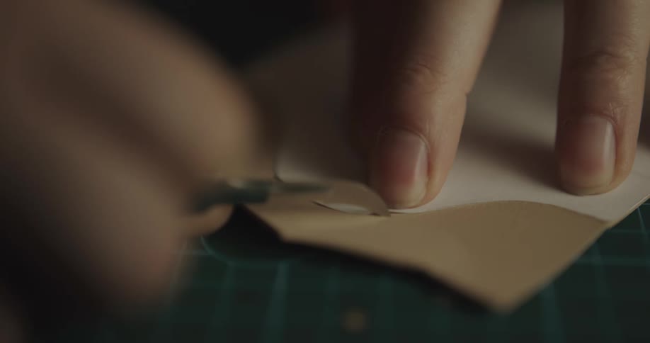 A man uses a small blade and a paper template to cut a small sheet of leather
