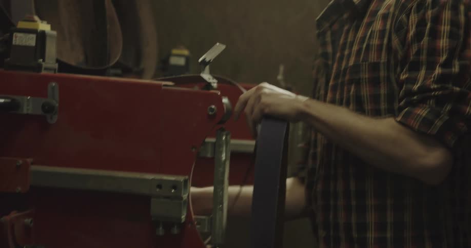 A man selects a sandpaper belt and begins to load it onto the power sander