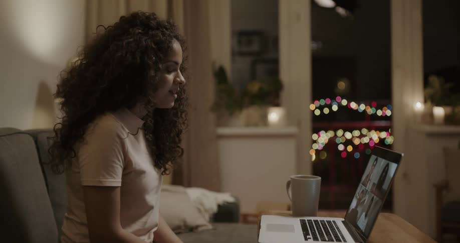 Young woman sitting at the couch and video calling a group of people on her laptop
