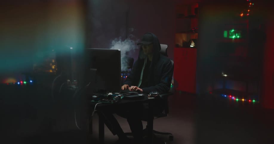 A man blows smoke as he sits in front of a computer and types