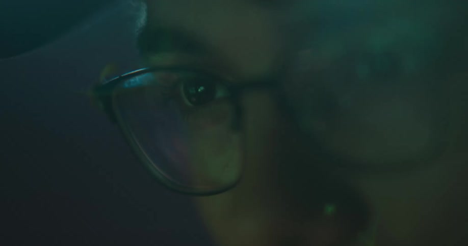 A person is sitting in a room and wearing glasses
