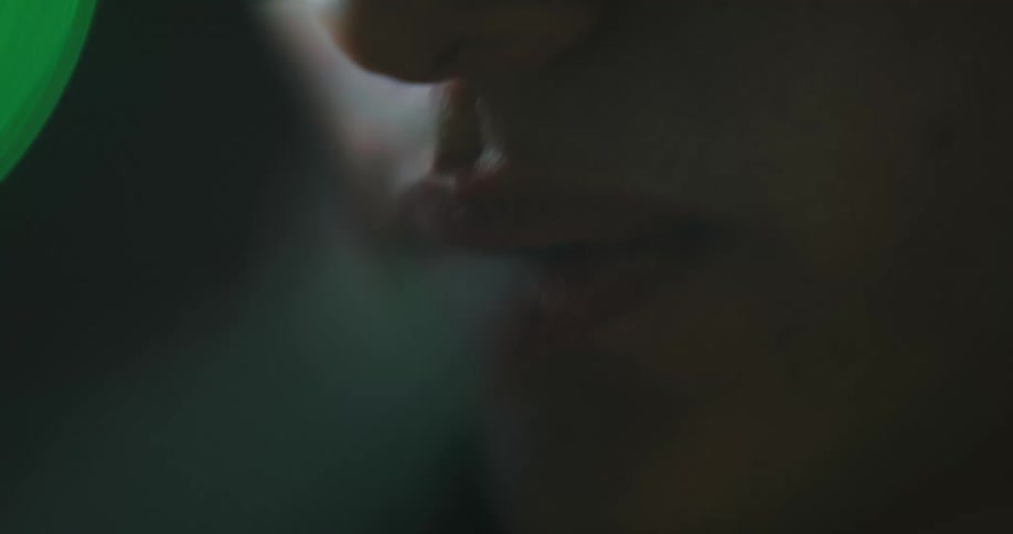 A teenage boy in the dark blows smoke out of his mouth