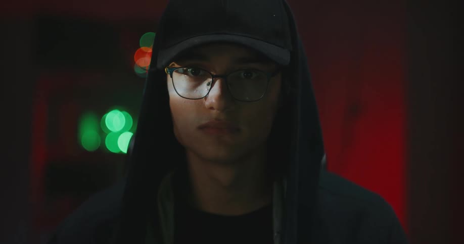 White teenager boy wearing eyeglasses hoodie and a cap in front of a screen