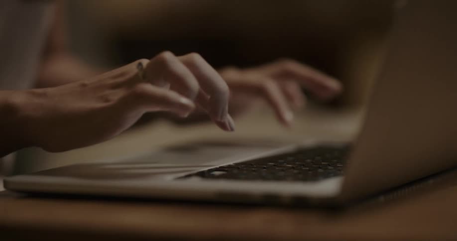A young woman types on a laptop while sitting at a desk