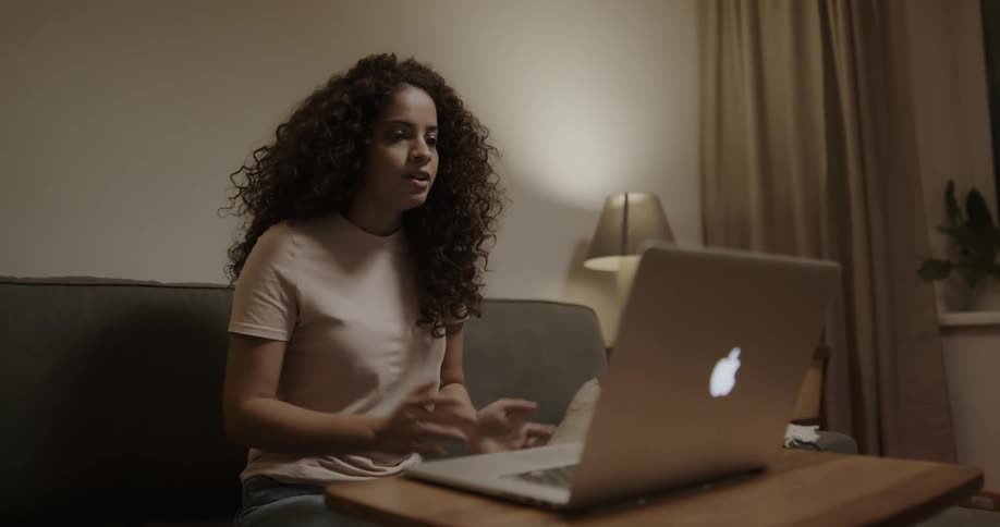 A woman sitting on a couch talking to a laptop webcam
