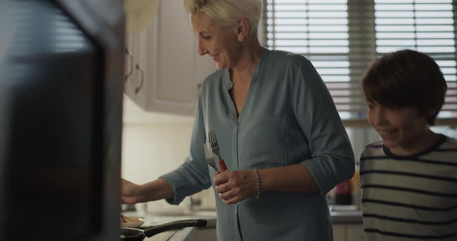 Grandson grabs food as grandmother cooks in kitchen
