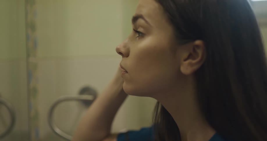 A woman in a bathroom standing in front of a mirror and putting on makeup