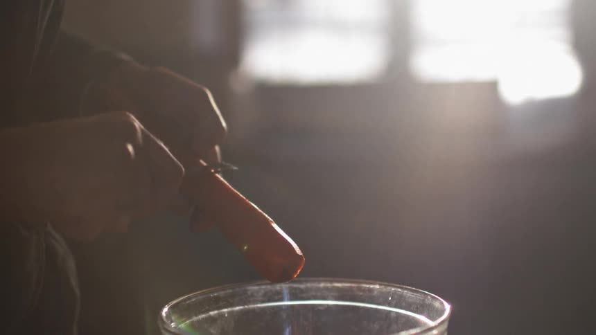 A person peels a carrot with sunlight pouring through a window