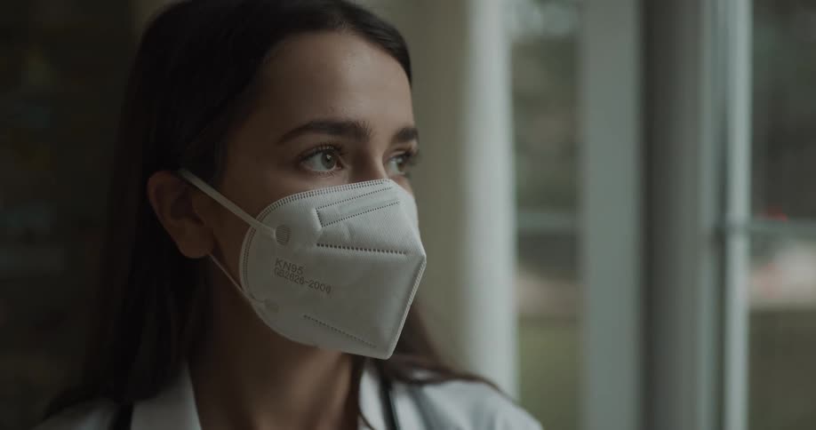 White woman wearing surgical mask looking through the window in a contemplative way